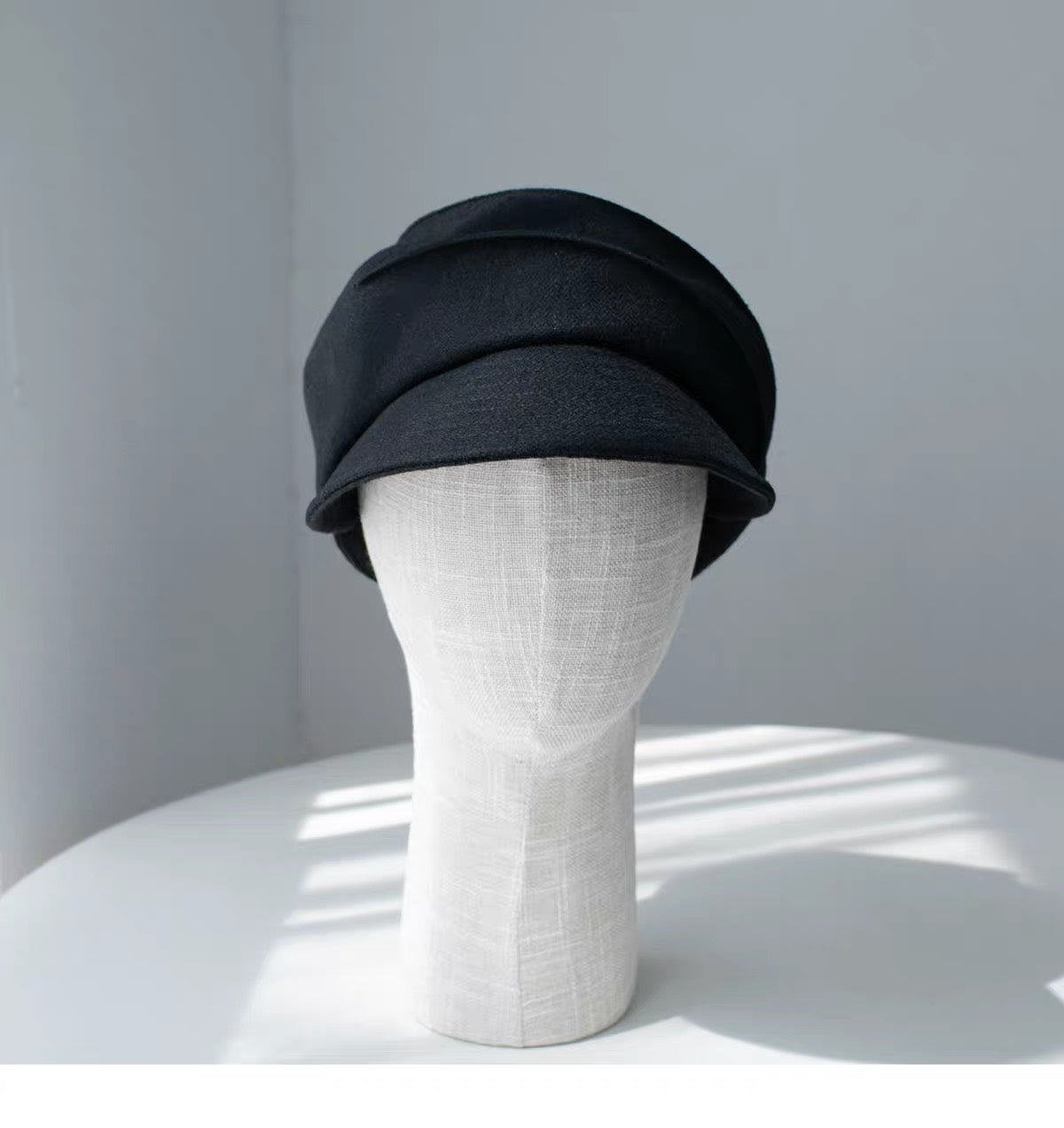 Black 100% wool newsboy cap shown from the front on a display form