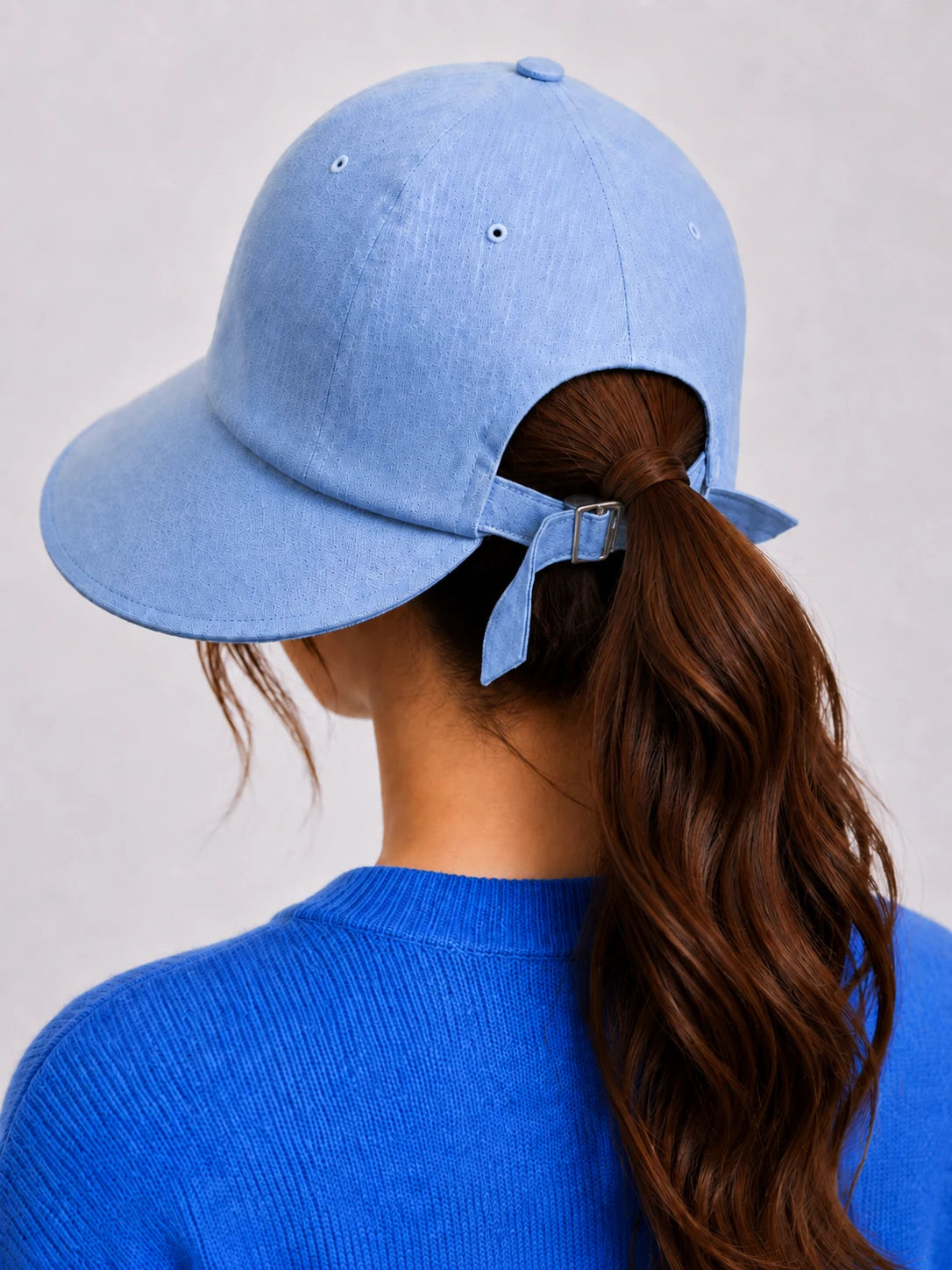 Back view of woman with long ponytail through light blue linen sun hat opening