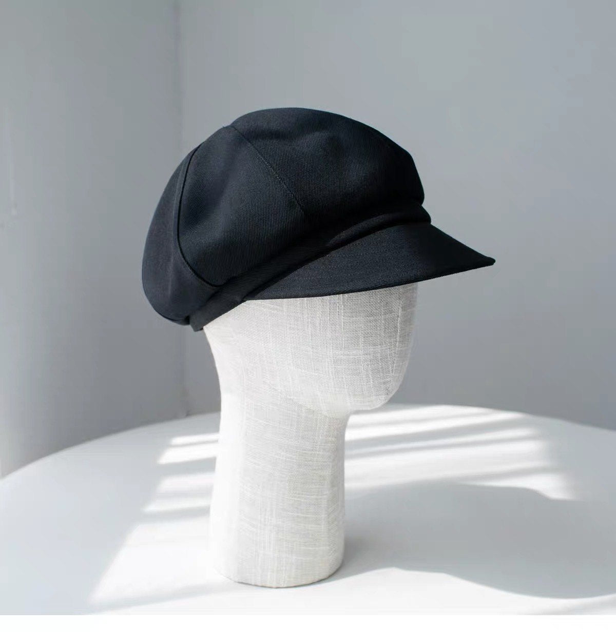 Black fine woven wool newsboy cap shown from the right front on a display form