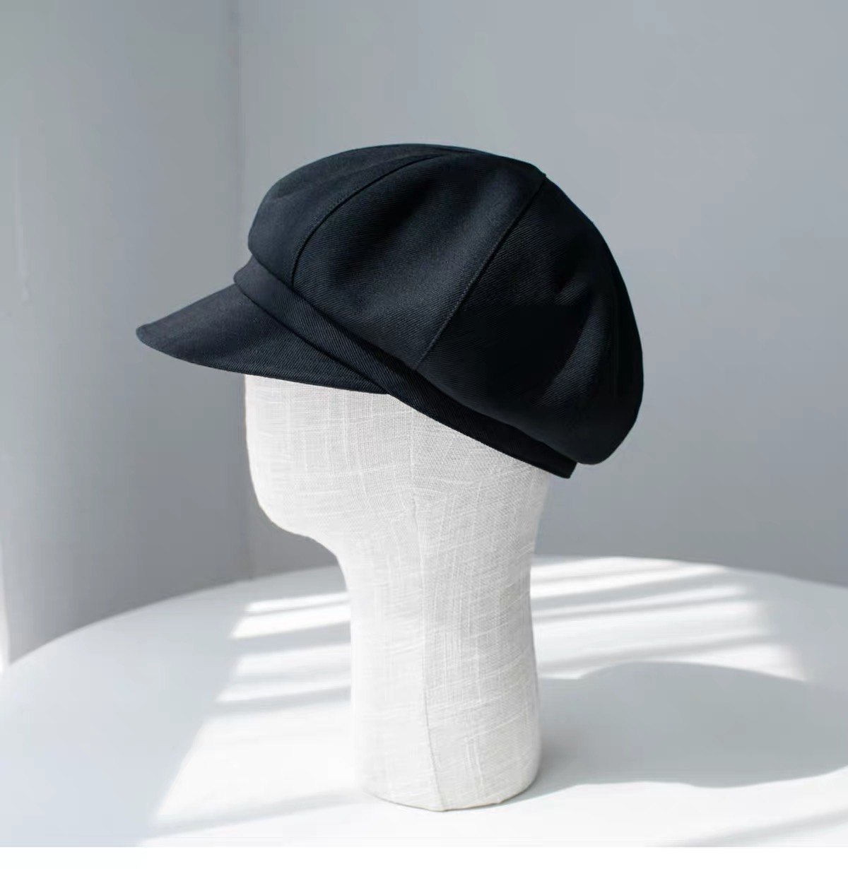Black fine woven wool newsboy cap shown from the left front on a display form