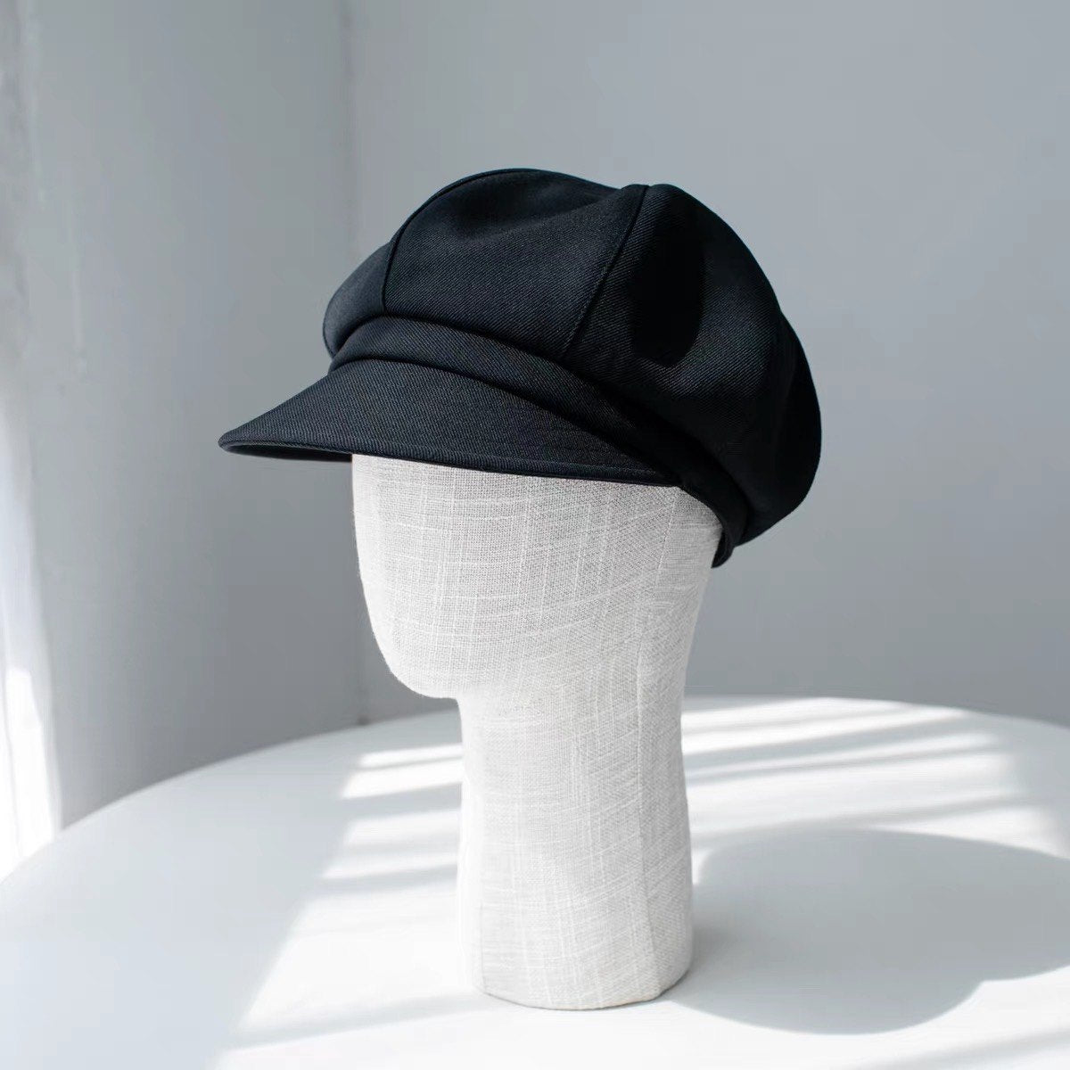 Black fine woven wool newsboy cap shown from the front on a display form