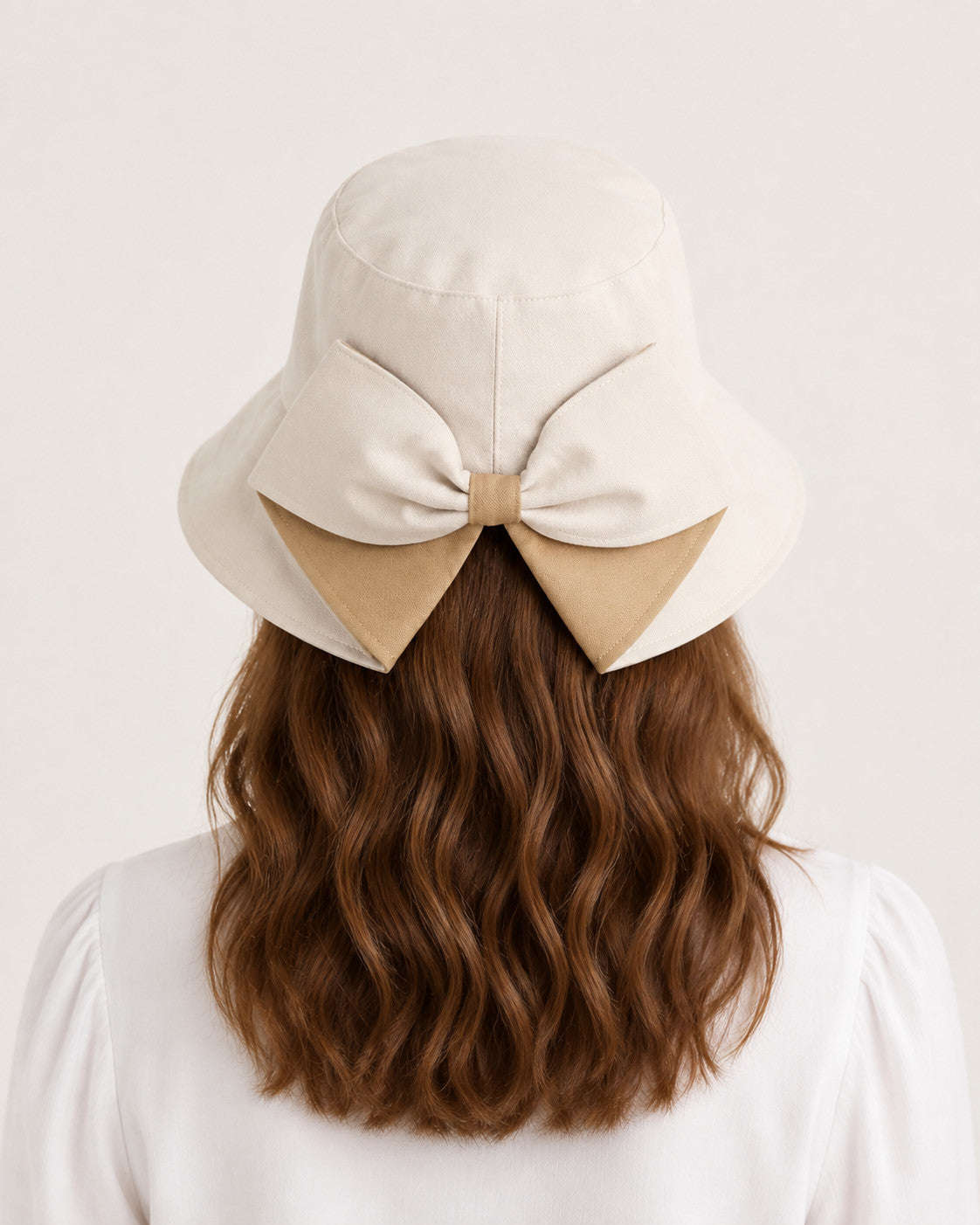 Rear view of woman wearing beige bucket sun hat with oversized camel bow