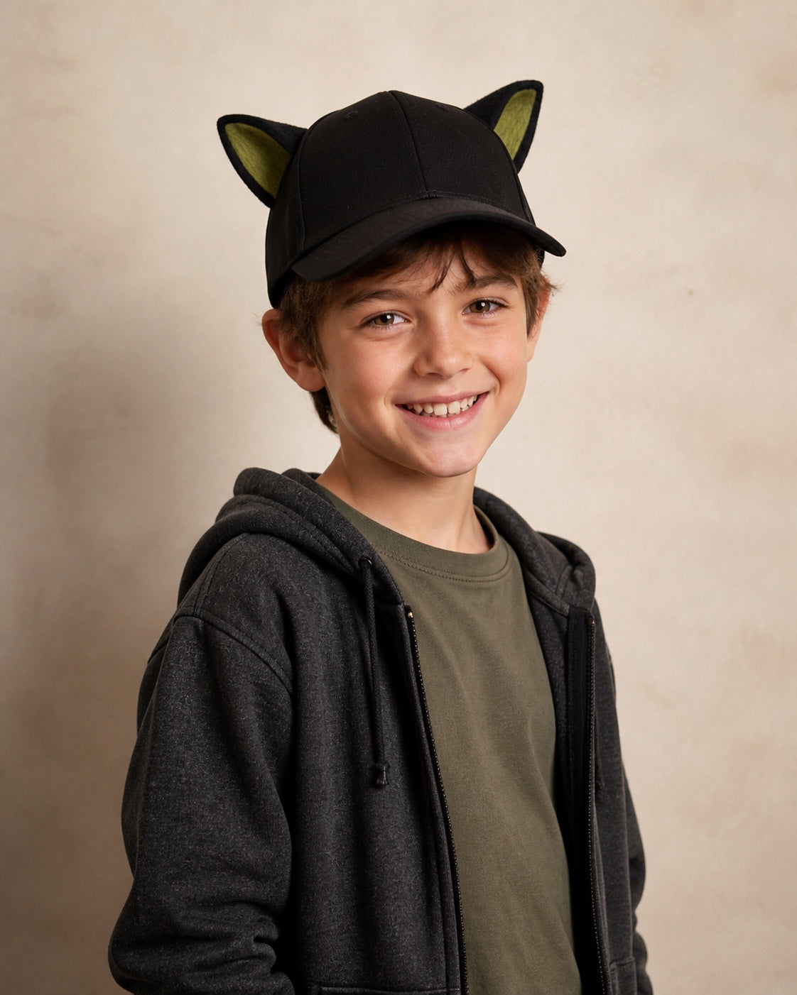 Child wearing the black animal-ear baseball cap with olive-green inner ears in an age-appropriate studio portrait