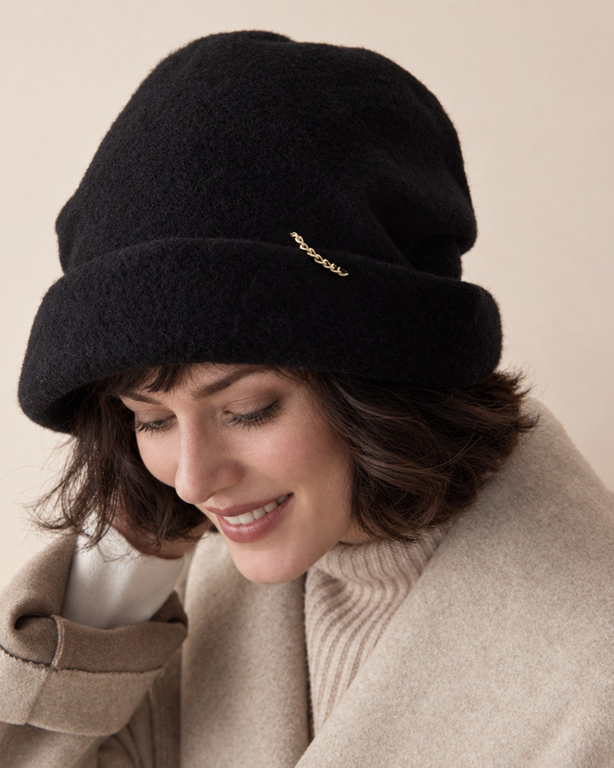 White female model wearing the Classic Black wool slouchy beret in a downward smiling studio view