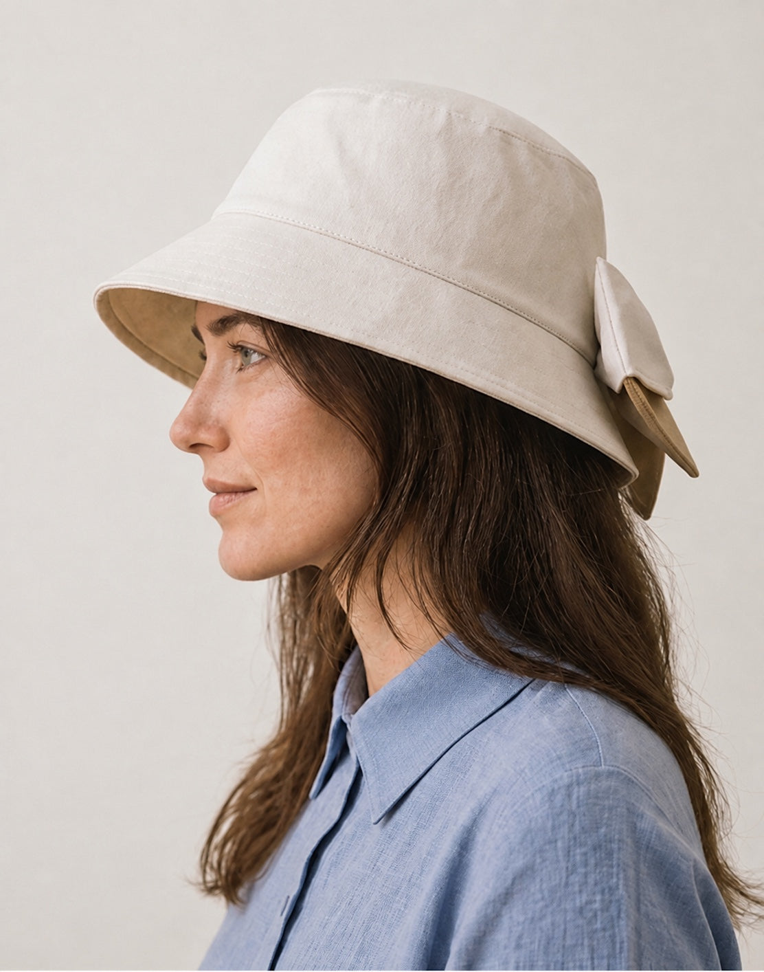 Side profile of woman wearing beige bucket sun hat with ivory and camel back bow