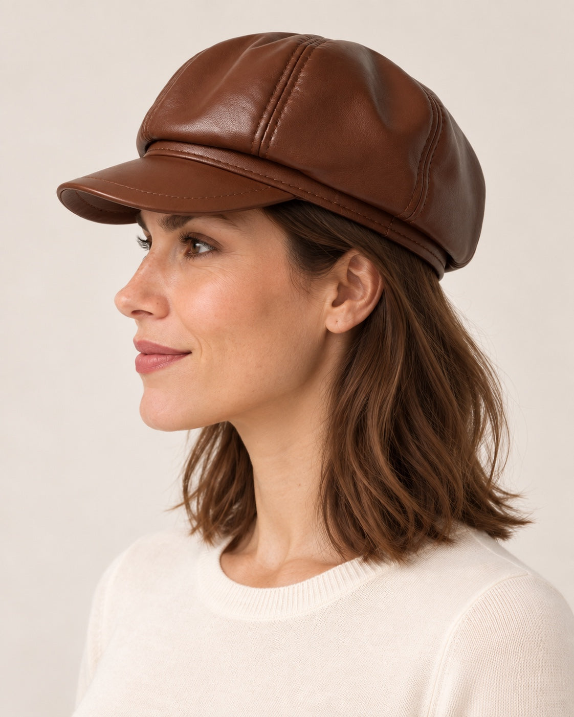 Woman in an ivory knit top wearing the brown genuine leather short-brim newsboy cap, side profile