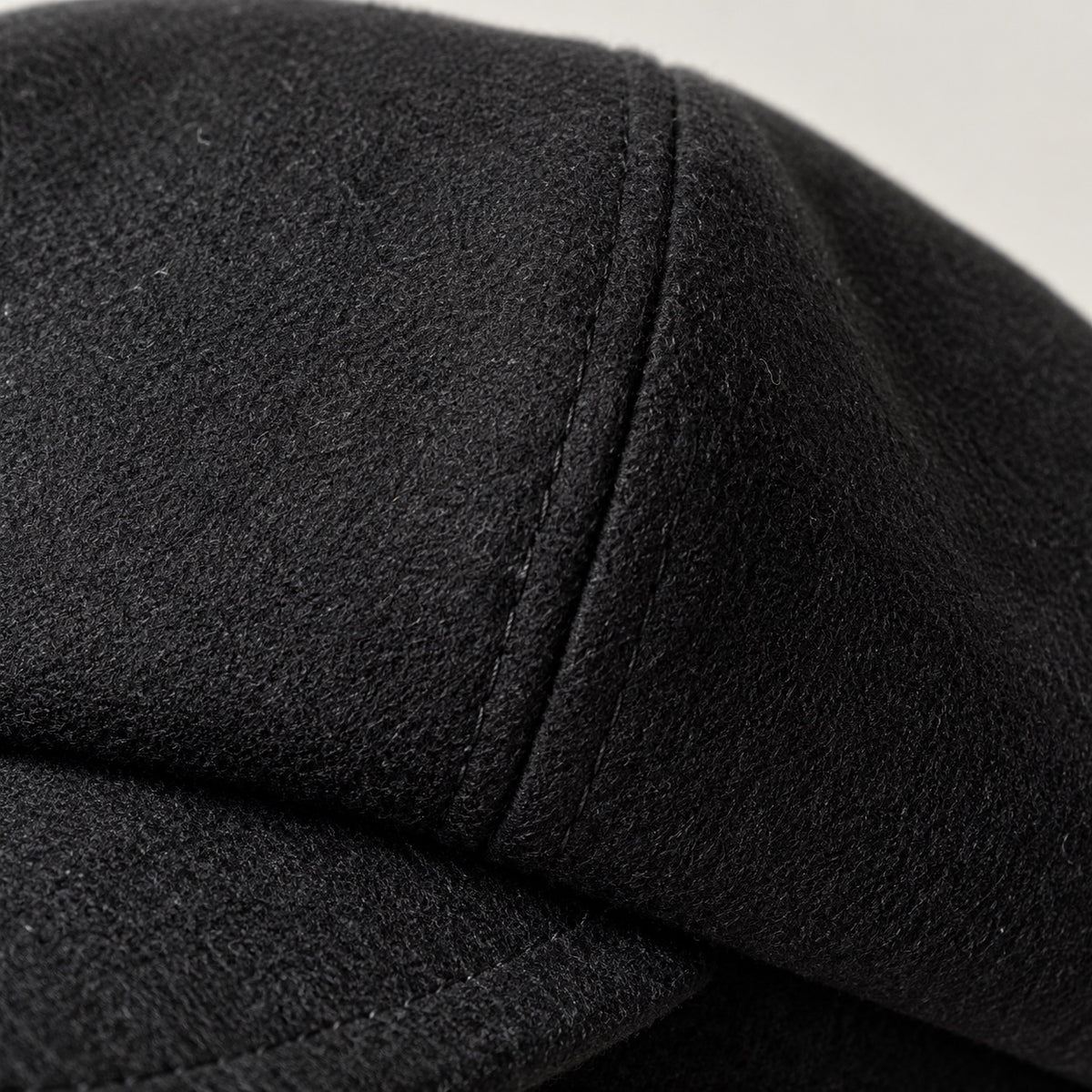 Black newsboy cap close-up showing textured crown fabric and panel stitching