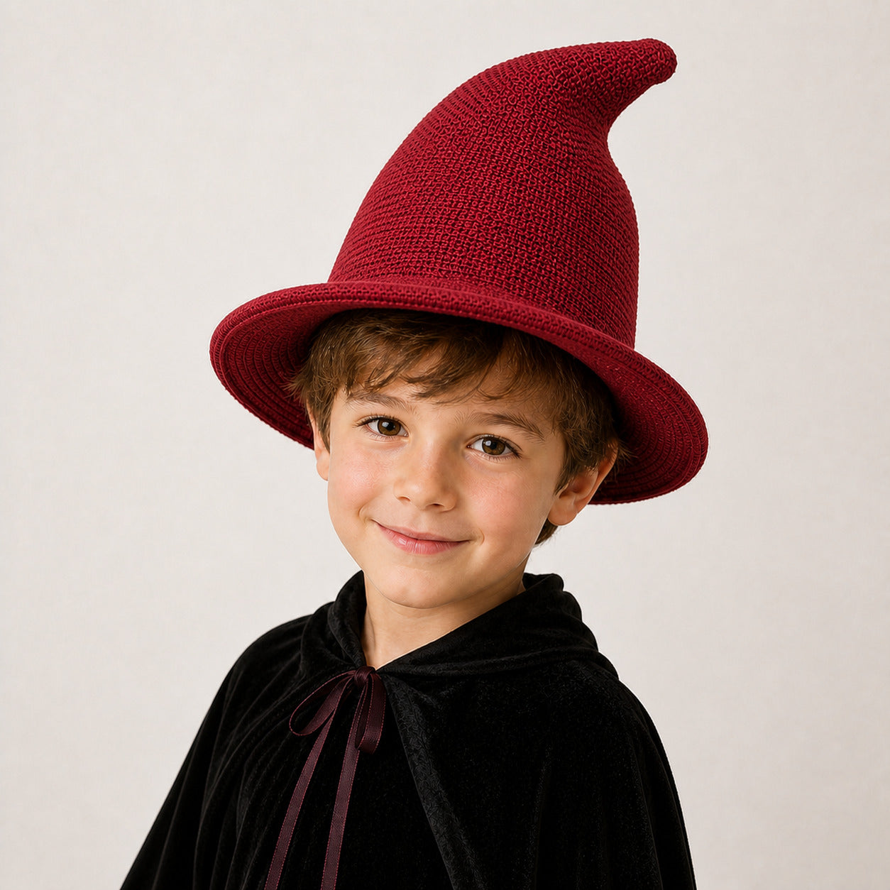 Boy wearing a burgundy knitted witch hat and Halloween wizard costume
