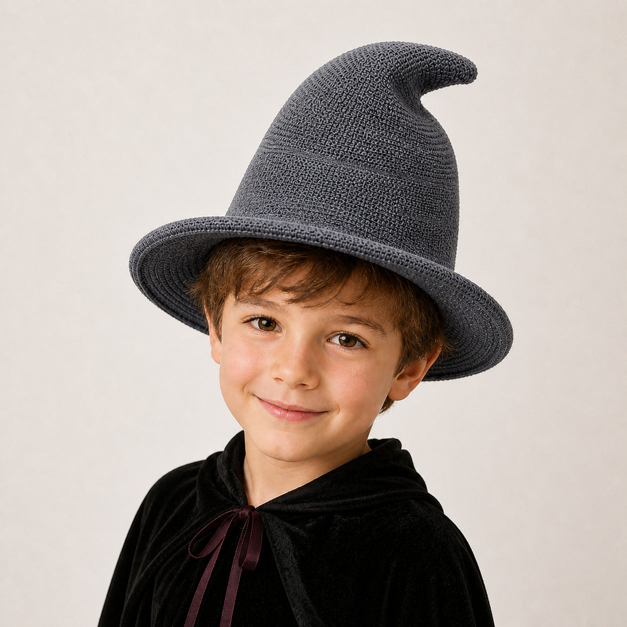 Boy wearing a dark gray knitted witch hat and Halloween wizard costume