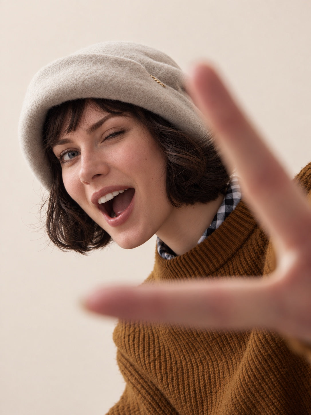 White female model wearing the Oat Almond wool slouchy beret in a playful studio pose