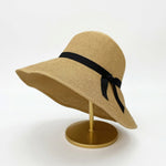 Foldable straw cloche hat with black ribbon bow on display stand
