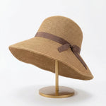 Foldable straw cloche hat with brown ribbon bow on display stand