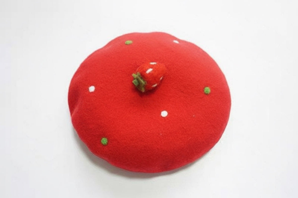 Red strawberry wool beret with white polka dots and green accents, angled view on white background