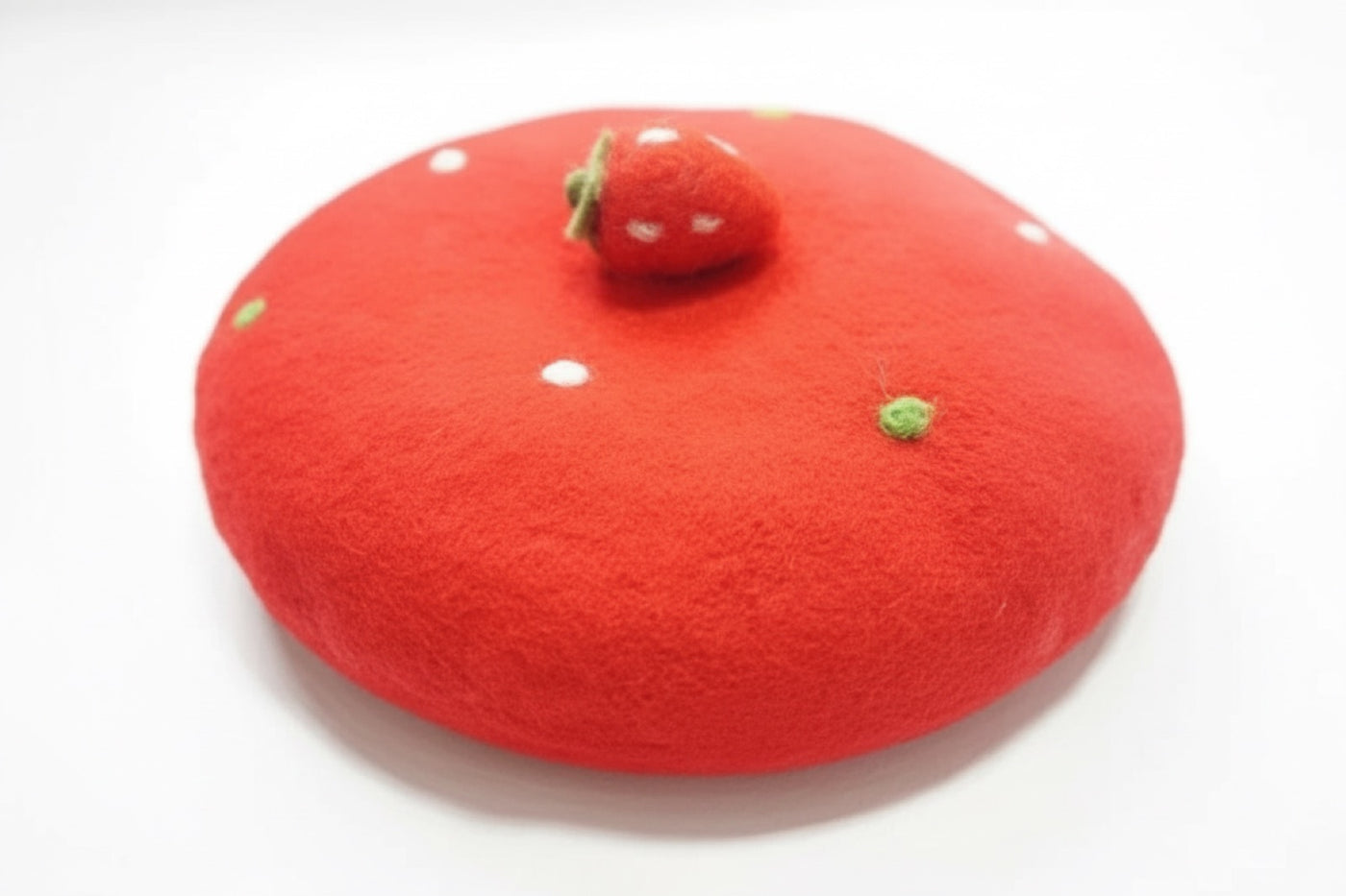 Red handmade wool beret with strawberry top decoration on white background