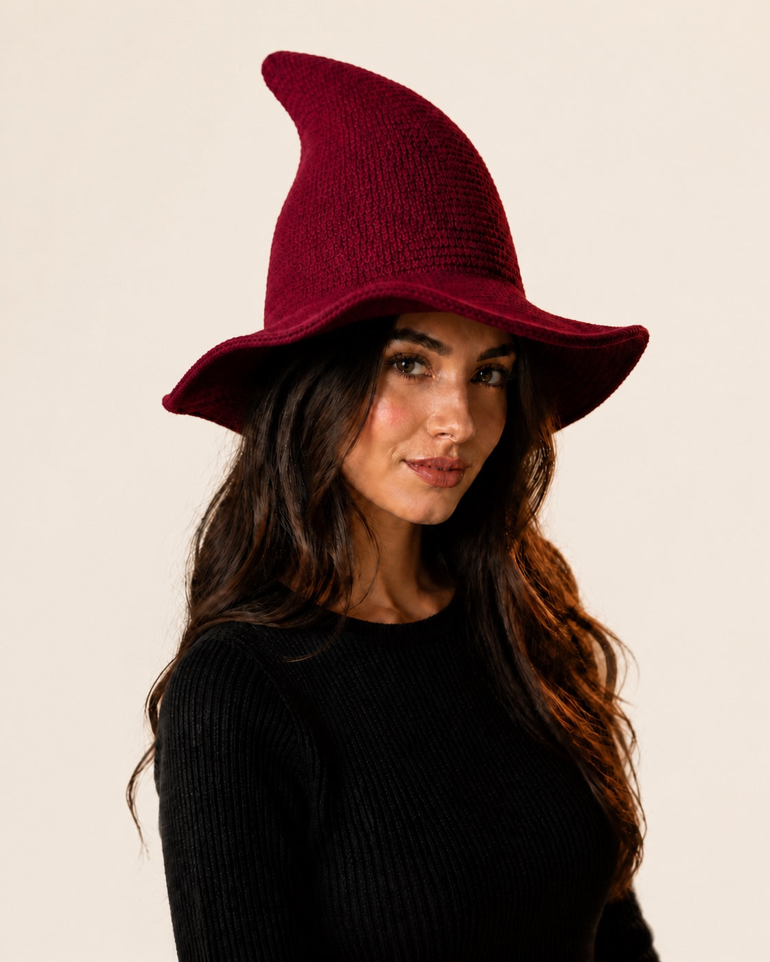Model wearing a burgundy knitted witch hat against an off-white studio background