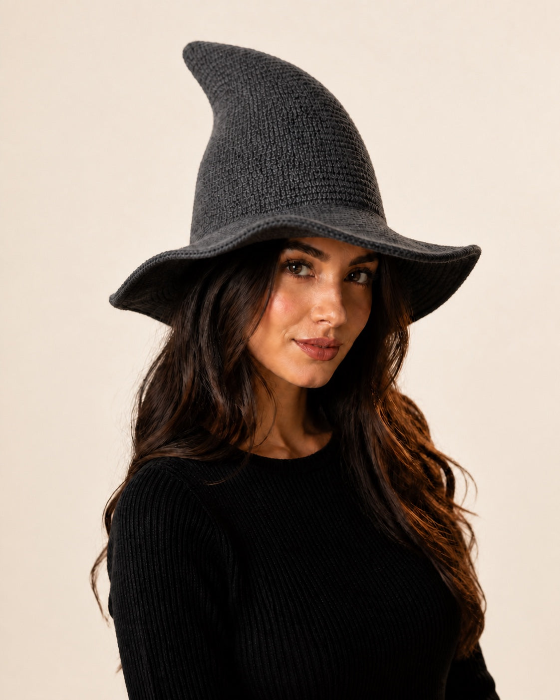Model wearing a dark gray knitted witch hat against an off-white studio background