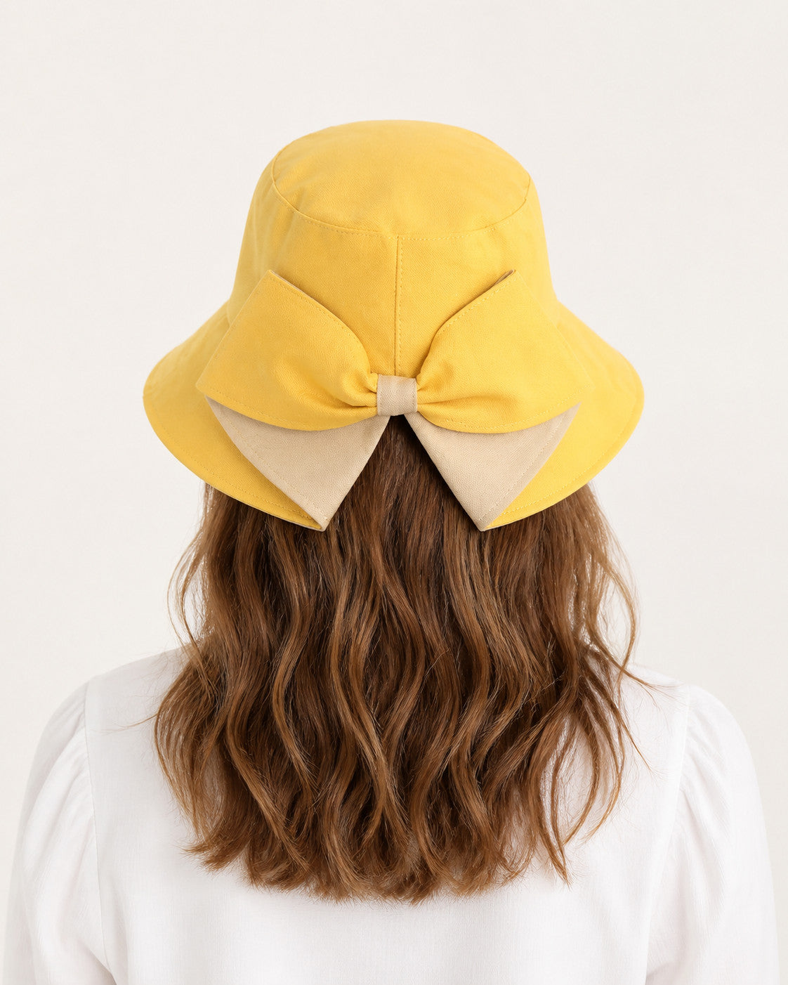 Rear view of woman wearing yellow bucket sun hat with oversized camel bow